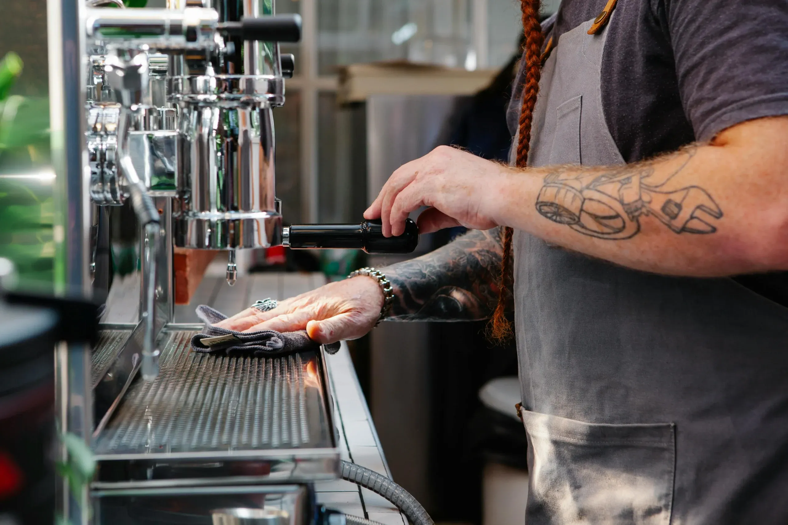 Camarero limpiando con un paño la rejilla de una cafetera de bar