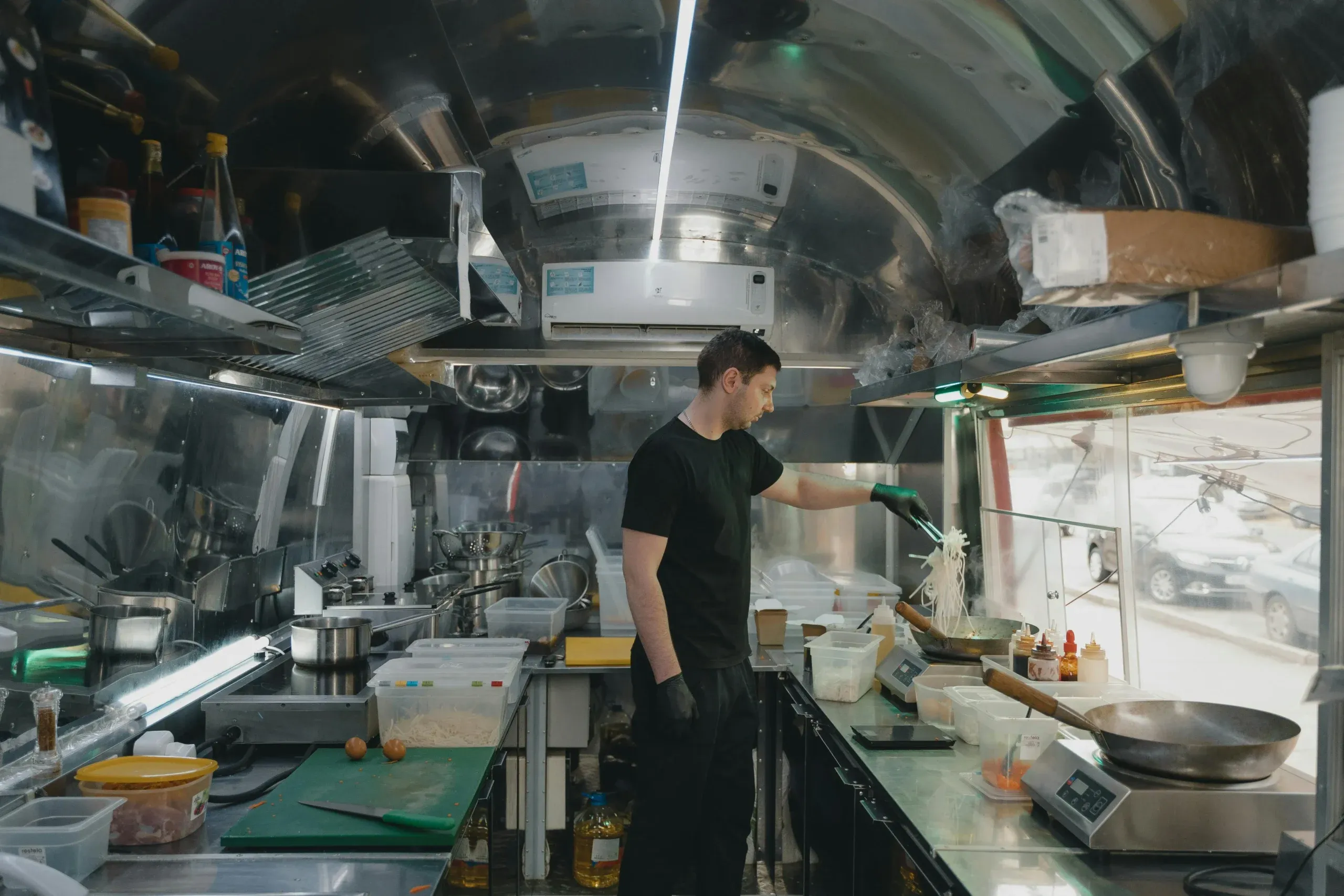 Cocinero salteando fideos en la cocina de un food truck forrada de acero inoxidable